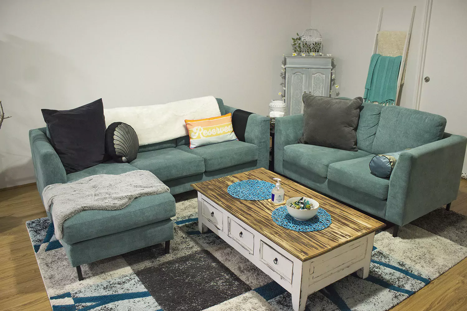 An alternative view of the second lounge room of Sudden Comforts accommodation. The couches are aqua in colour and are inviting with pillows and blankets draped over them. The room also has decorative house plants, a coffee table and a bowl of snacks.