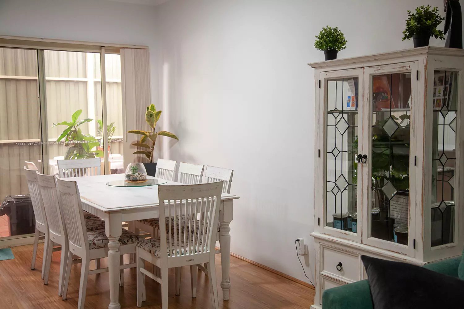 The image is of the dining room of the Sudden Comfort's accommodation. It overlooks the patio and the room is furnished with comfortable white washed furniture with a 'beach town' vibe