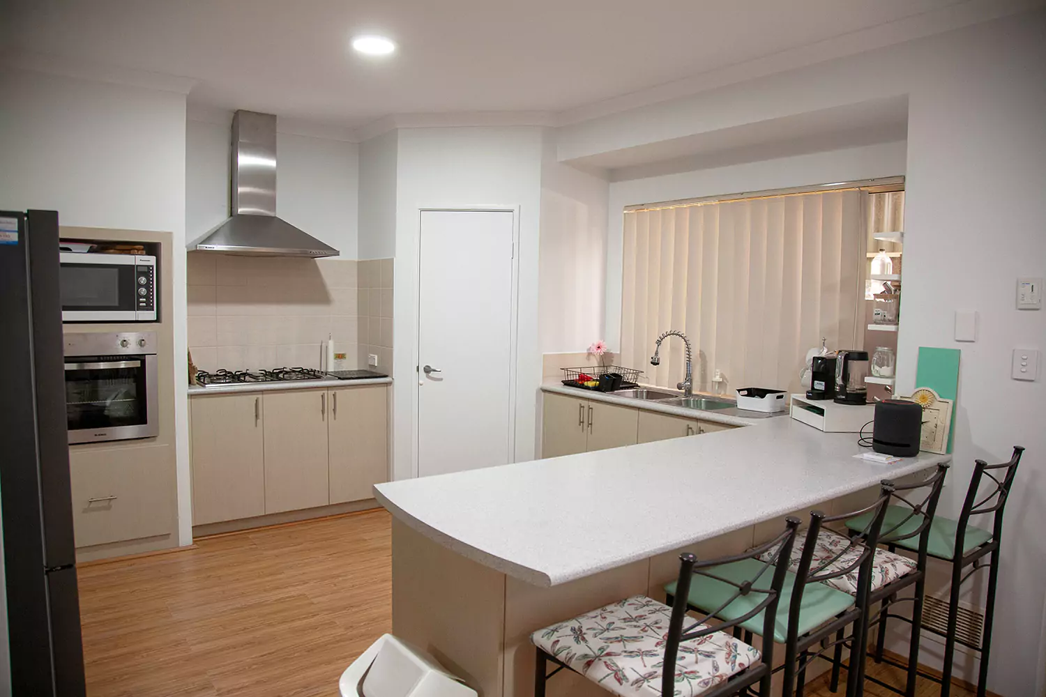 The 2nd photo angle of the kitchen of the Sudden Comfort's accommodation. There are comfortable seating options across from the bench, a large clean prep area for cooking and many modern cooking appliances.
